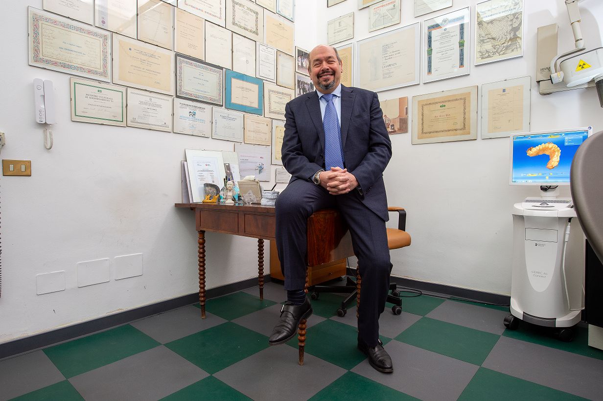 Il Prof. Bruno Grilli seduto nel suo studio, con gli attestati appesi alle pareti